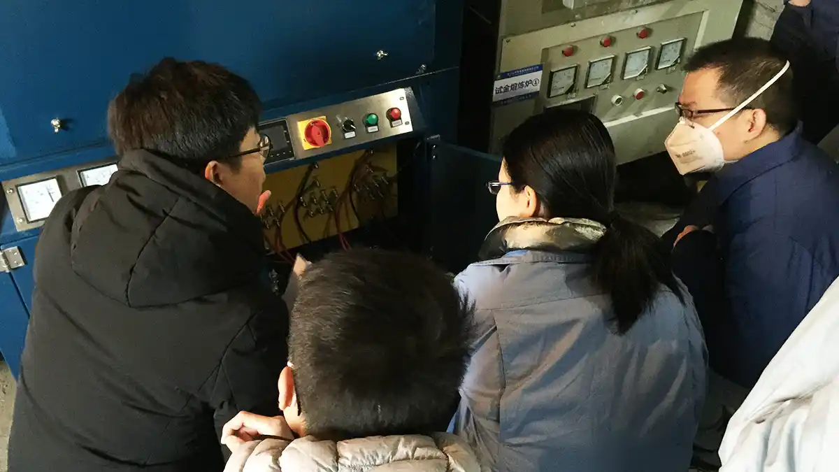 Qingdao Decent Group engineer providing hands-on training to a group of operations of Hunan Shuikoushan Nonferrous Metals Group Co., Ltd. on operating fire assay fusion furnace, focusing on the control panel and technical aspects.