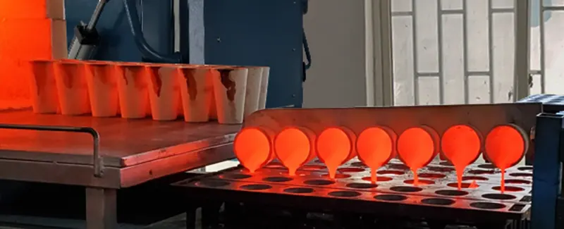 Molten material being poured from hot DECENT fire assay crucibles into iron molds during a high-temperature casting process.