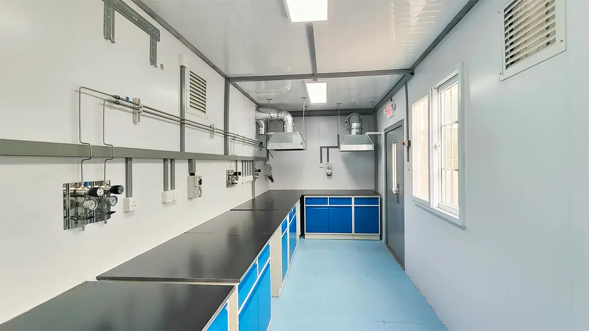 Interior of a DECENT Graphite AAS Analytical Hub, showing a rightward view of the AAS testing area with lab benches, blue cabinets, gas lines, and two overhead exhaust hoods.
