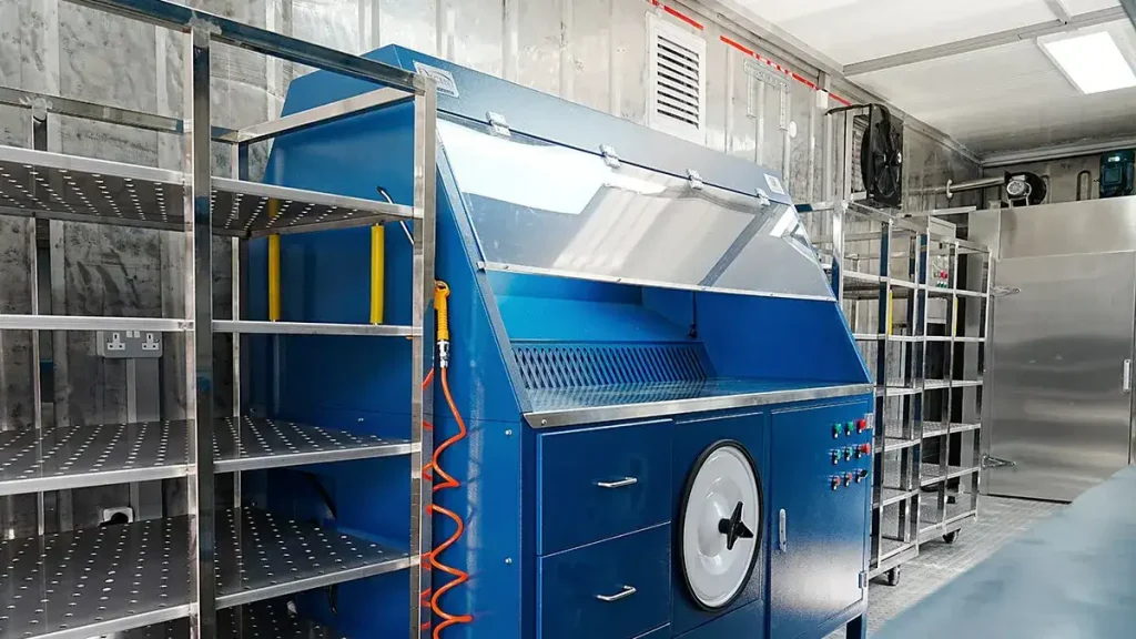 Interior of a DECENT Malaysia Container Laboratory Project 2024 Drying and Initial Preparation Lab, showing a blue sample preparation station with a hose, stainless steel shelving, and a large stainless steel drying oven.