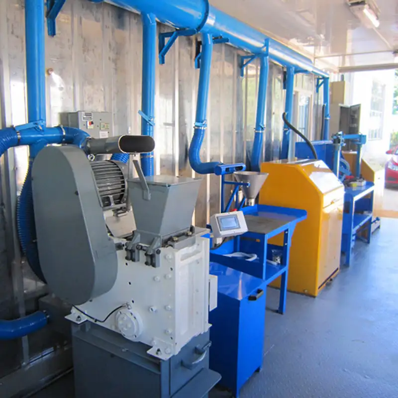 Inside a containerized laboratory, showing a grey jaw crusher and other blue mineral sample preparation machines connected by overhead ventilation ducts.