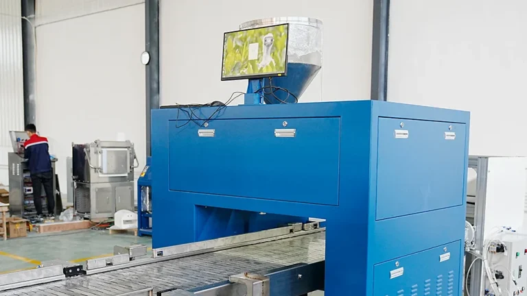 A blue DECENT fully automated fire assay system with a conveyor belt and a monitor displaying a user interface, in a clean industrial setting
