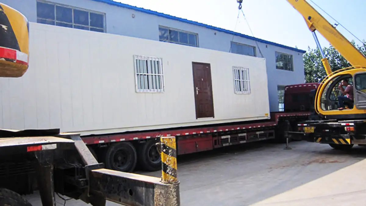 A large white shipping container, a fully-equipped mineral sample preparation laboratory by Qingdao Decent Group, is carefully loaded onto a truck by a crane.