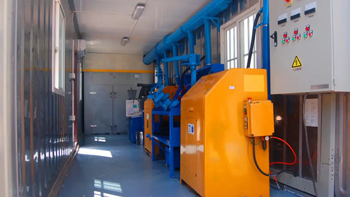 Interior of a mobile containerized laboratory showing mineral sample preparation equipment, a ventilation system, and an electrical control panel.