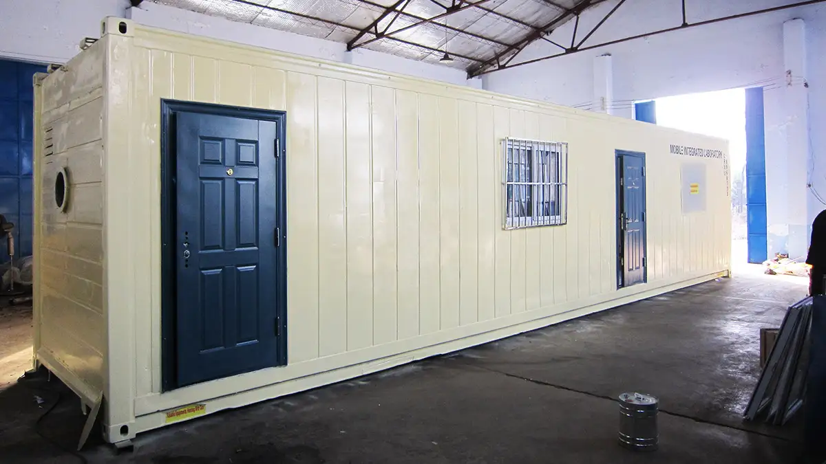 Revolutionary Container laboratory of sample preparation: 2015 South Korea Project 1 An exterior view of a cream-colored container laboratory of sample preparation with dark blue doors, inside a warehouse.