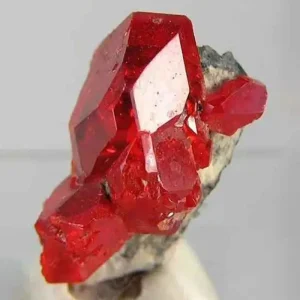 5 Stunning The Minerals Types That Will Amaze You - Nature's Hidden Treasures 24 A cluster of brilliant, translucent red realgar crystals, a toxic arsenic sulfide mineral, on a light gray matrix.