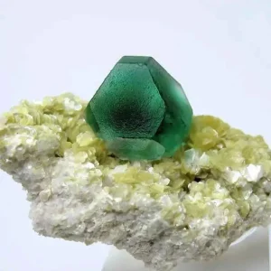 5 Stunning The Minerals Types That Will Amaze You - Nature's Hidden Treasures 32 A translucent green fluorite crystal with a dodecahedral shape, resting on a matrix of smaller yellowish-white crystals.