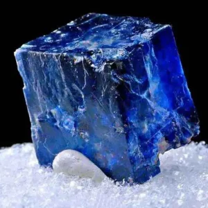5 Stunning The Minerals Types That Will Amaze You - Nature's Hidden Treasures 29 A large, translucent blue halite crystal, a form of rock salt, with a cubic shape, resting on a bed of white crystalline particles.