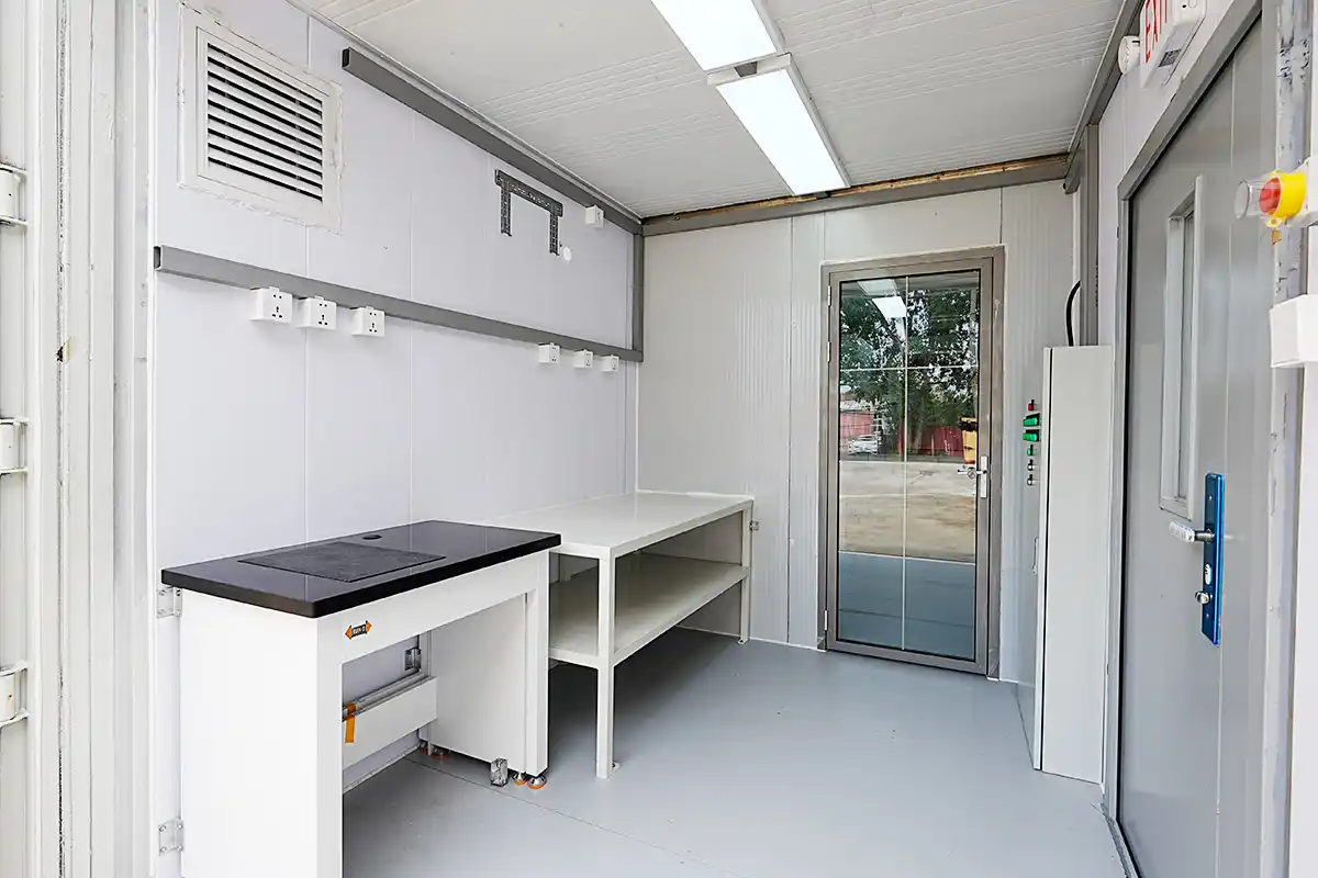 The clean, white interior of a DECENT chemical analysis lab, showing a workbench with a black top and a glass door.