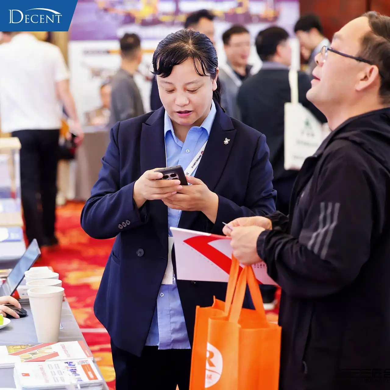 Qingdao Decent Group sales rep consulting client at 2026 Gold Tech Conference booth, discussing fire assay automation and lab solutions for gold mining labs